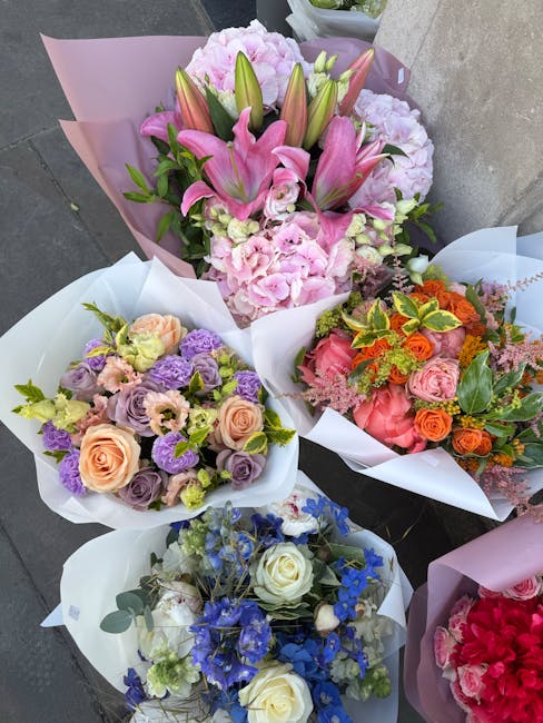 A collection of five bouquets of fresh flowers arranged for floral delivery or gifting, laid out on a grey surface. The top bouquet features pink lilies, pink carnations, and green foliage, wrapped in