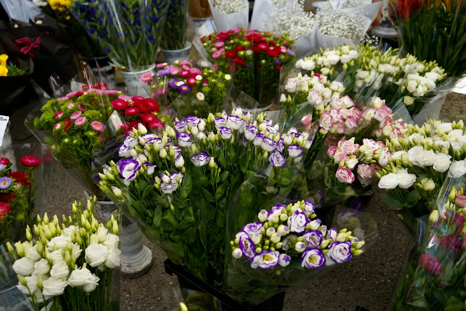 A display of fresh floral bouquets arranged on a counter, featuring a variety of flowers including purple and white lisianthus, pink and white roses, red and pink daisies, and other mixed blooms. The 